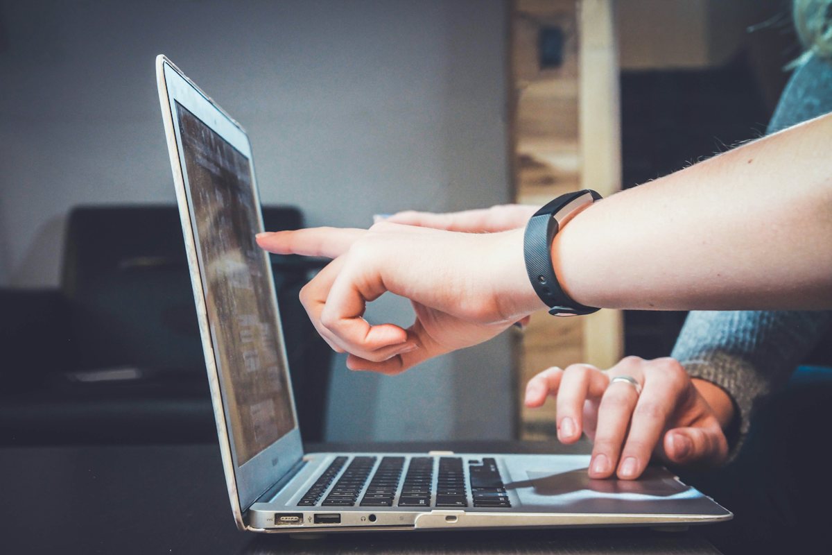 A person pointing at a laptop screen while another follows along